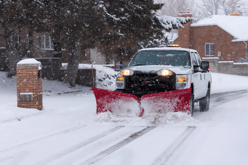 White pickup truck with red snow plow clearing snowy residential street