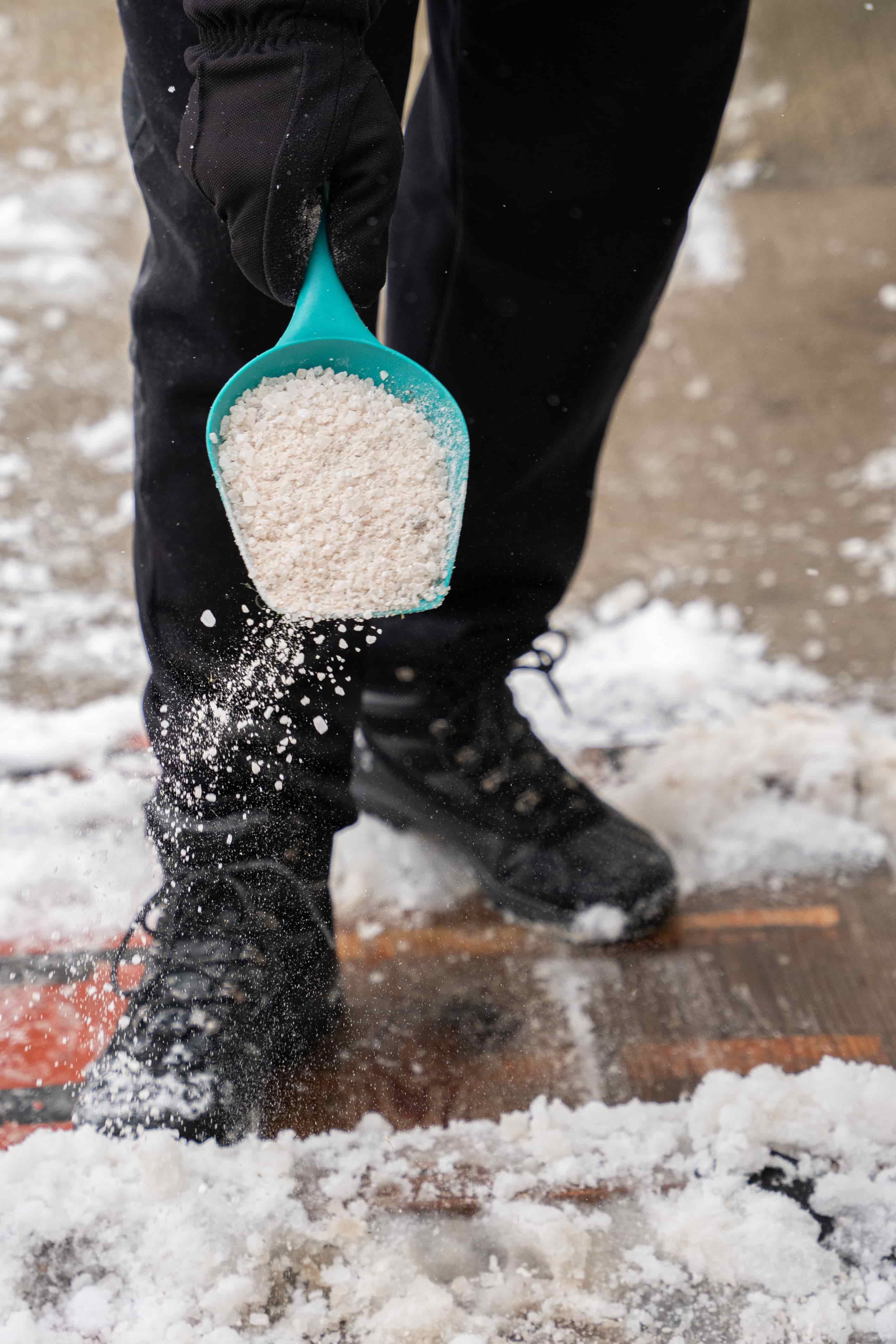Person spreading ice melt on a snowy sidewalk during snow removal