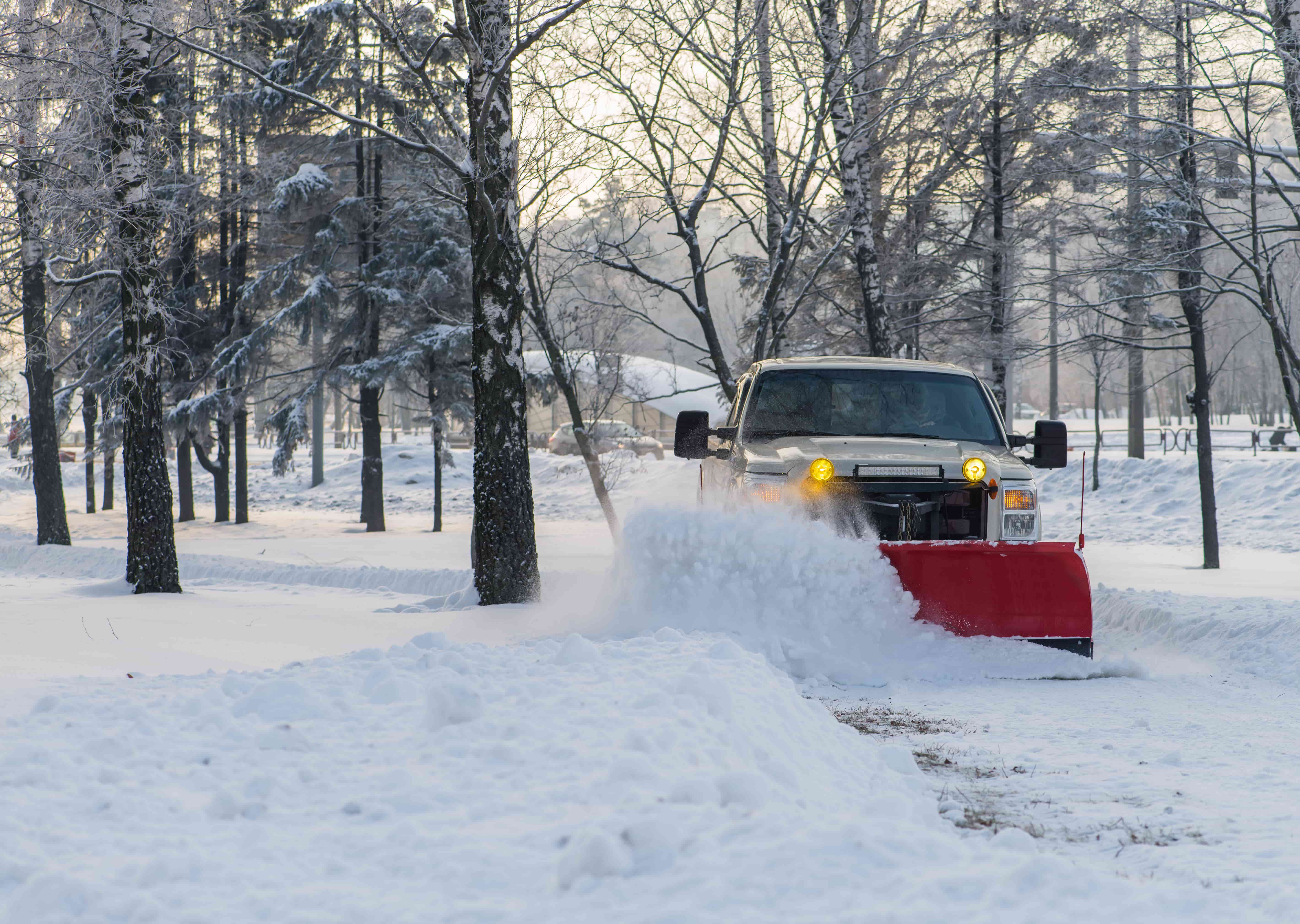 Truck with red plow clearing snow from a path during winter